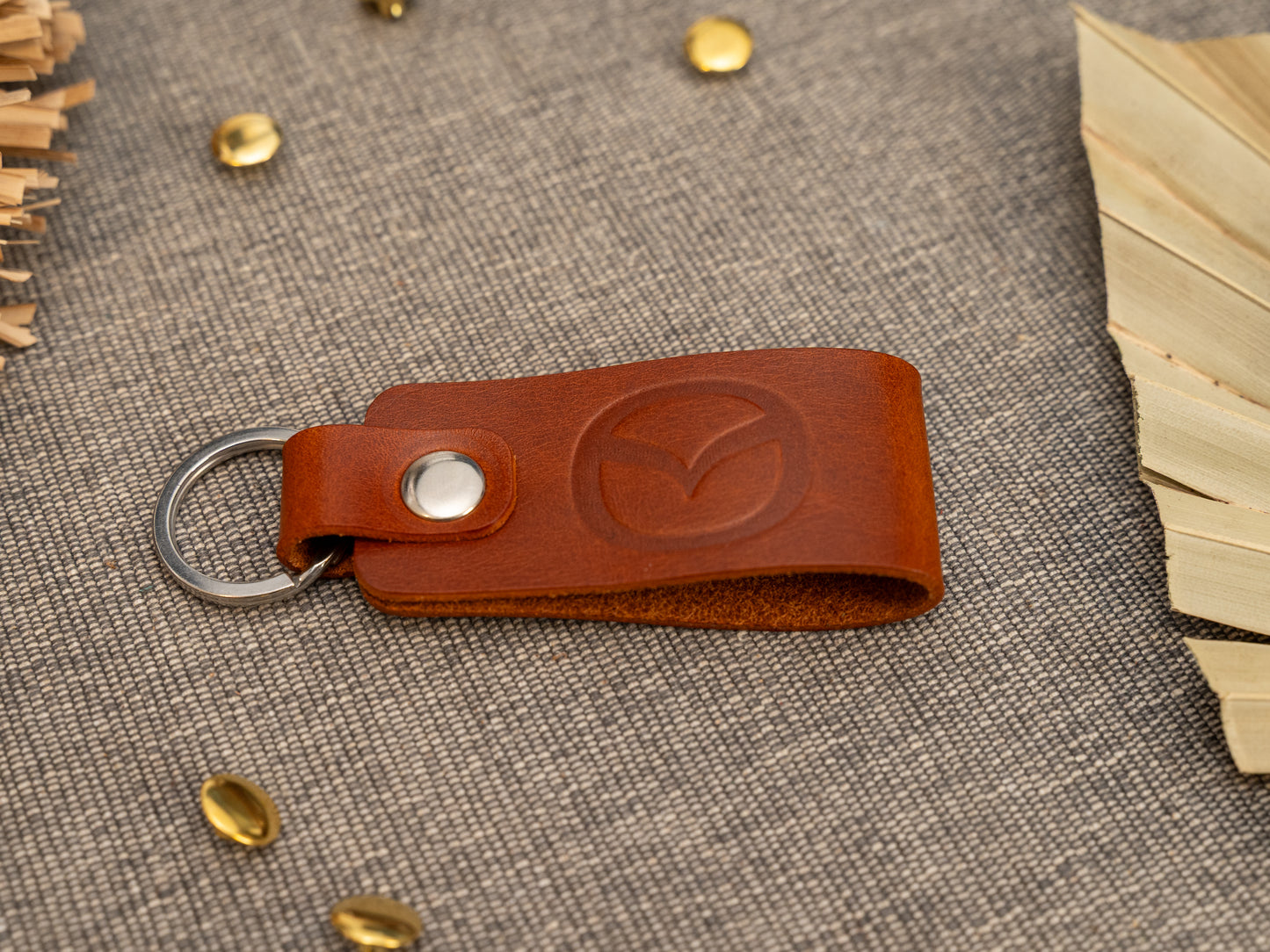 Folded tan leather keyring/keychain with the Mazda car logo debossed on it. Made from full grain leather with stainless steel split ring and rivet.