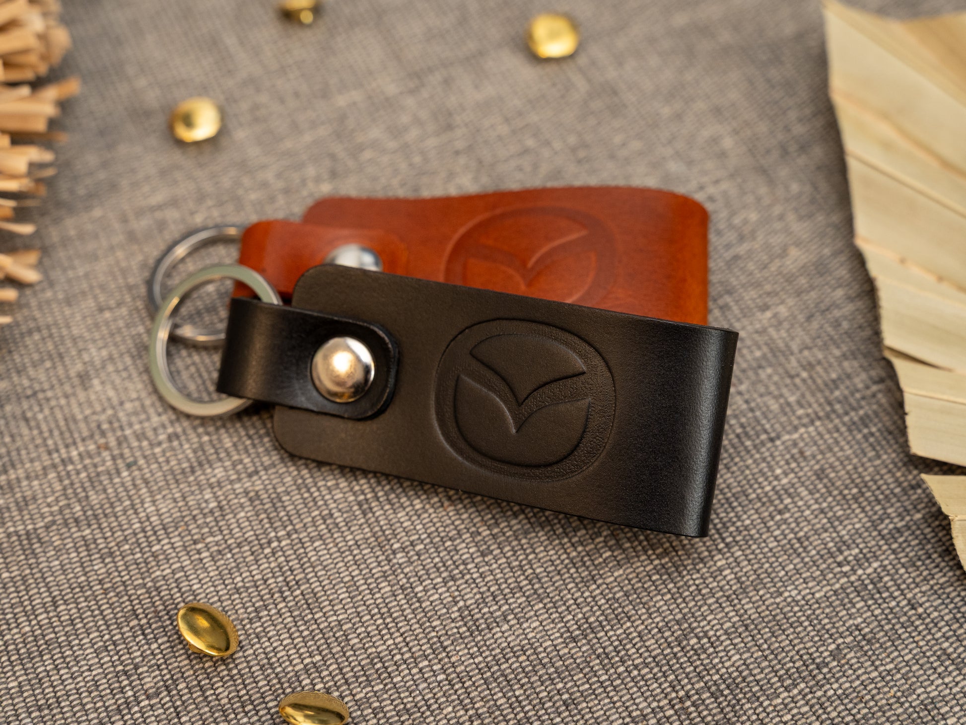 Folded black and tan leather keyrings/keychains with the Mazda car logo debossed on them. Made from full grain leather with stainless steel split ring and rivet.