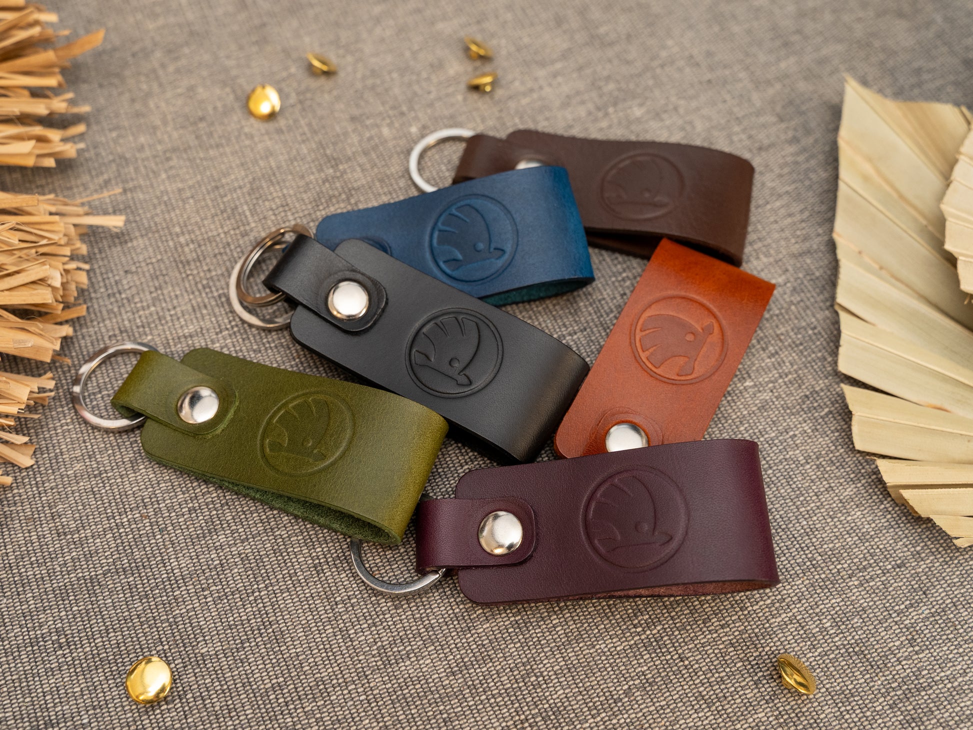 Several keyrings with a folded design in various colours such as tan, olive green, navy blue, dark brown, black and red keyrings/keychains embossed with the Skoda car logo. Stainless steel split ring and rivet.