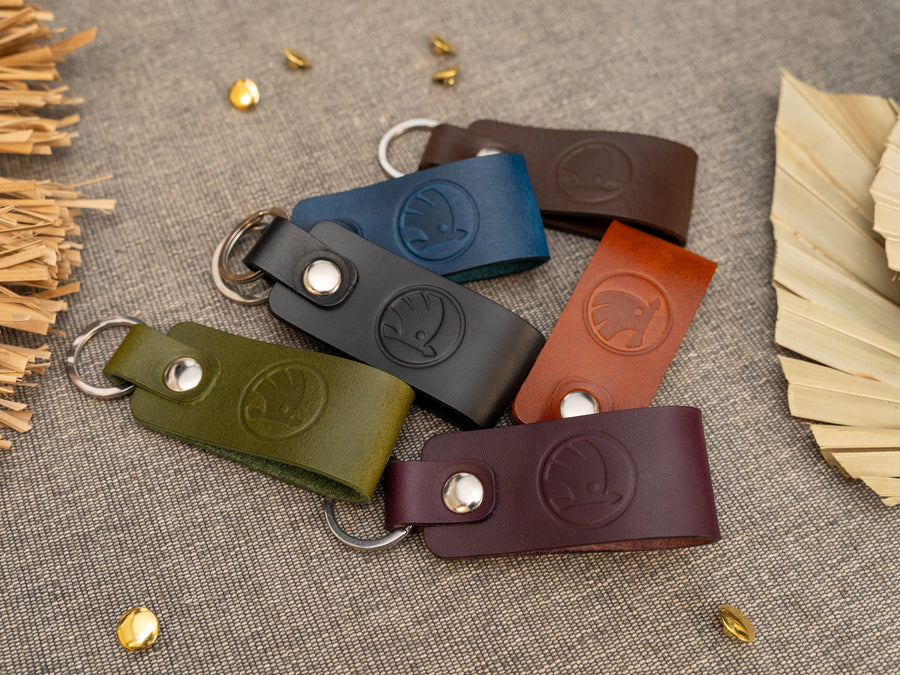 Several keyrings with a folded design in various colours such as tan, olive green, navy blue, dark brown, black and red keyrings/keychains embossed with the Skoda car logo. Stainless steel split ring and rivet.