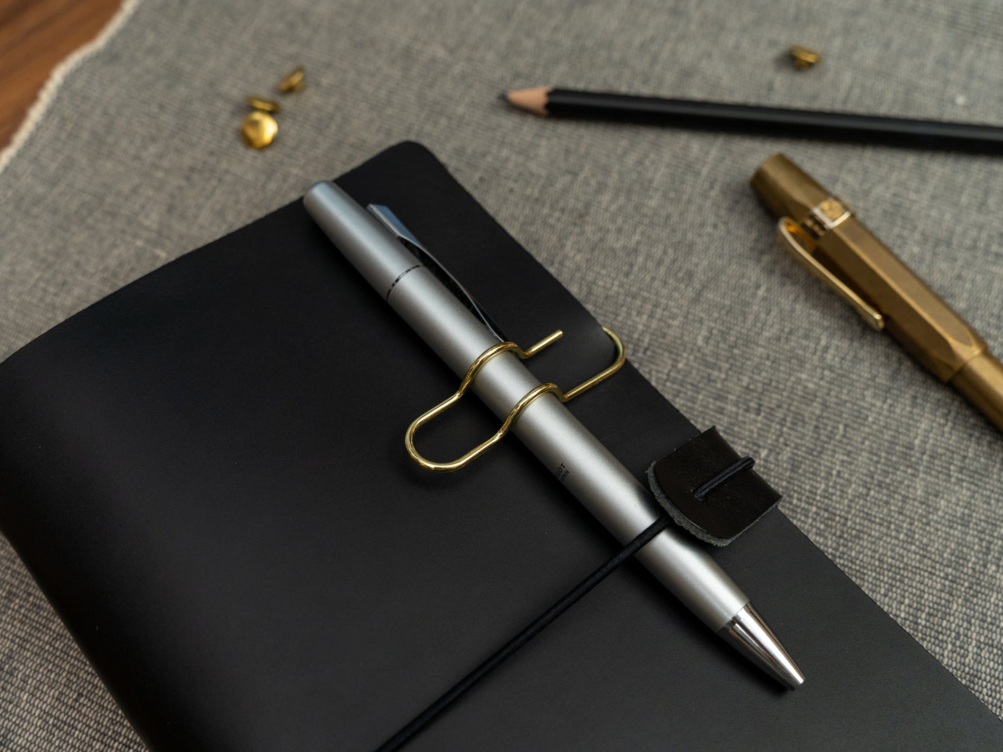 A silver ballpoint pen held on to a black leather notebook with a gold clip.