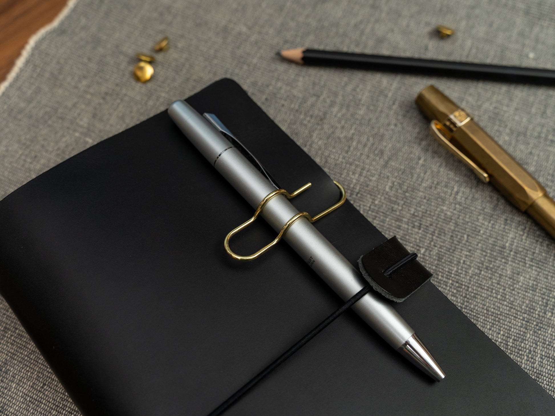 A silver ballpoint pen held on to a black leather notebook with a gold clip.