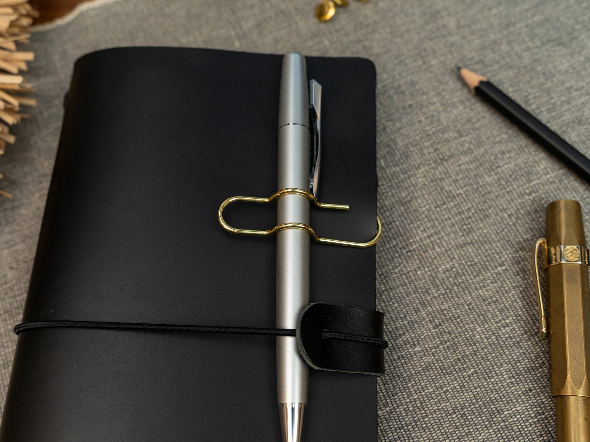 A silver ballpoint pen held on to a black leather notebook with a gold clip.