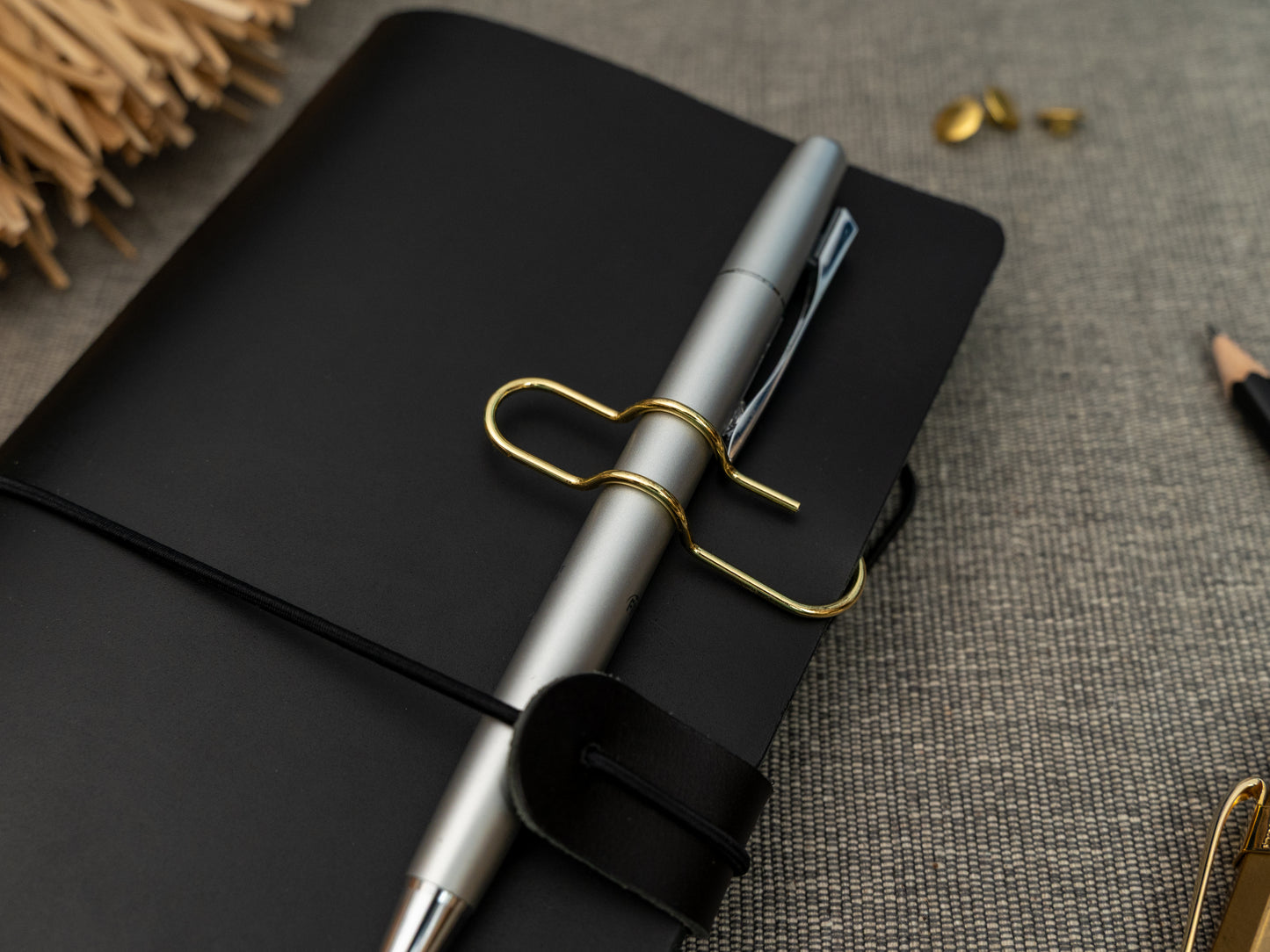 A silver ballpoint pen held on to a black leather notebook with a gold clip.